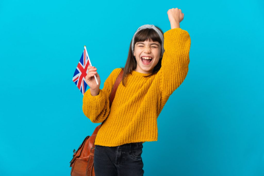 Otrok z britansko zastavo veselo praznuje uspeh pri učenju angleščine.