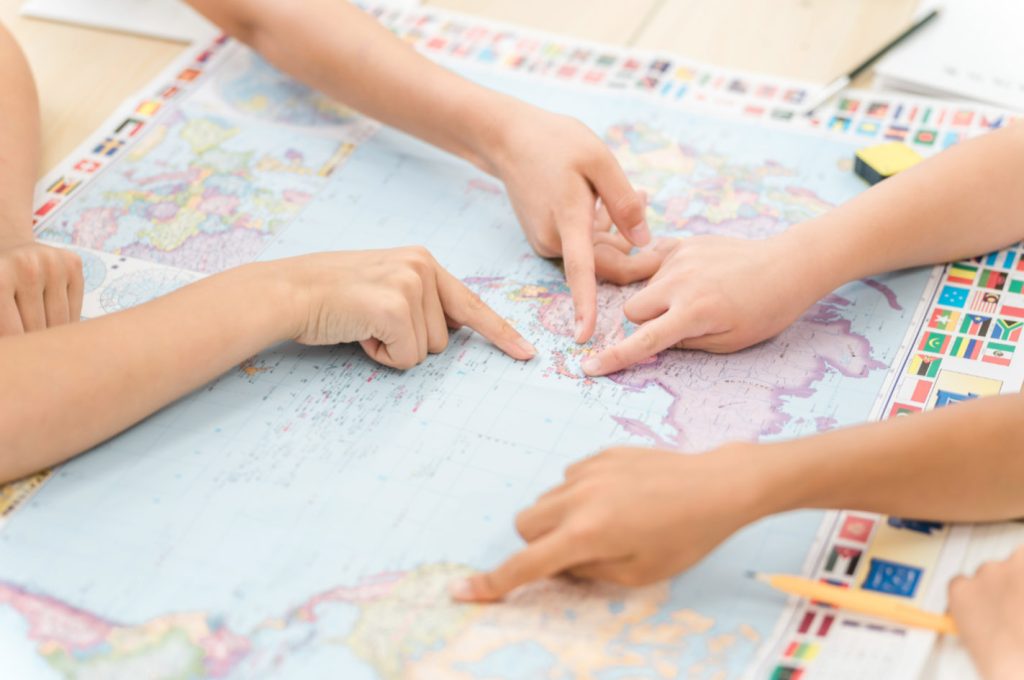 Otroci skupaj raziskujejo zemljevid sveta kot simbol globalnih priložnosti, ki jih prinaša znanje angleščine